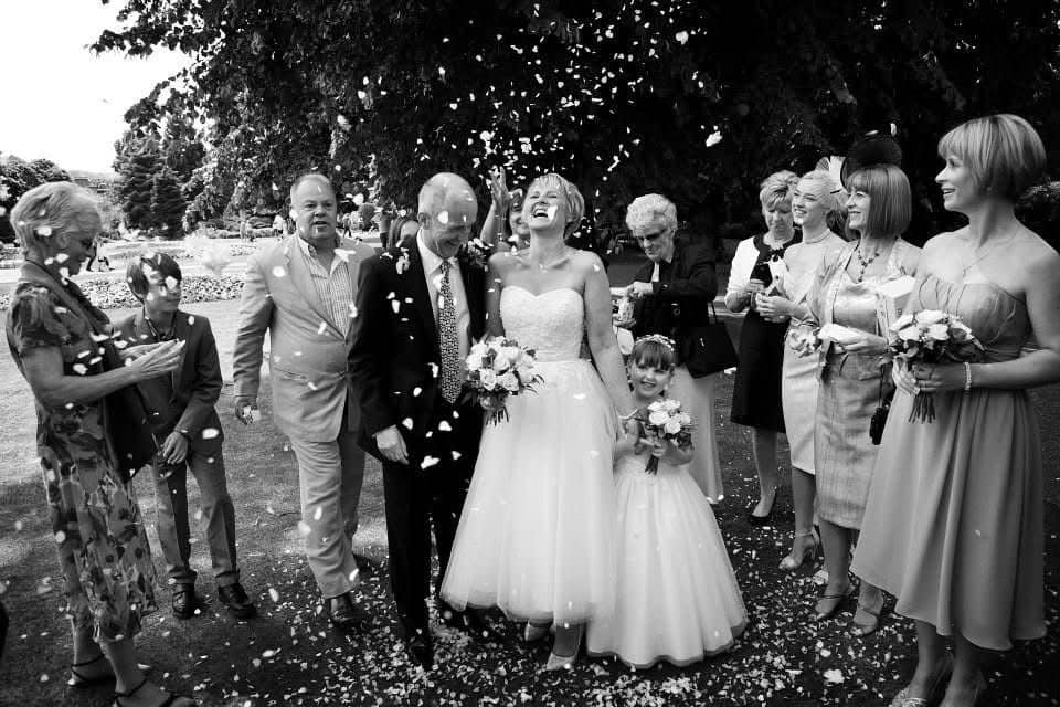 Joyful black and white confetti moment after outdoor wedding ceremony
