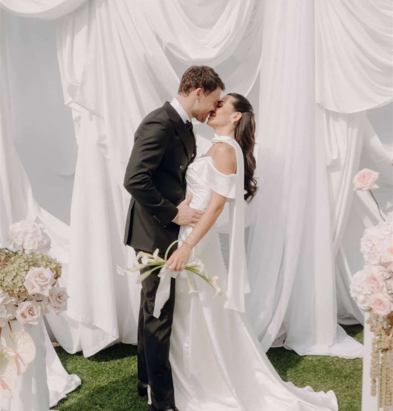 Romantic couple kiss at elegant white ceremony with pink floral arrangements