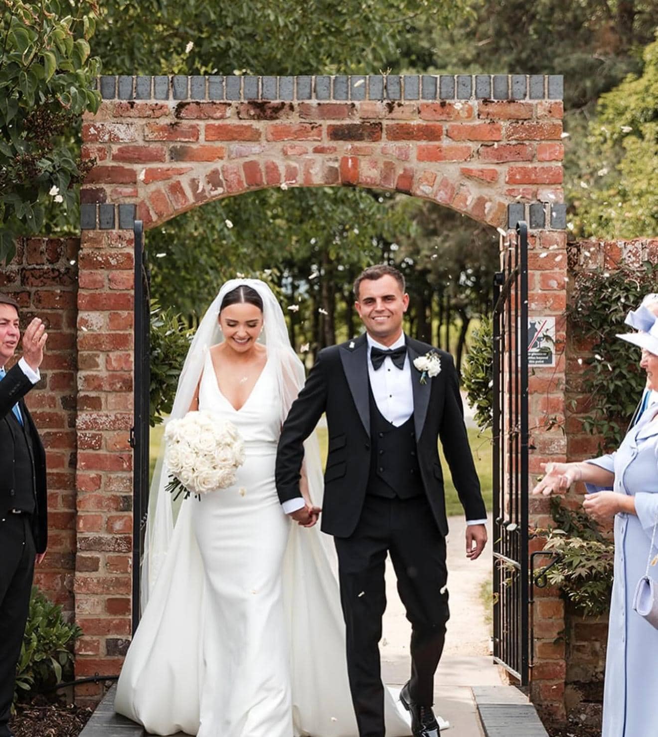 Joyful newlyweds walking through brick archway with guests cheering